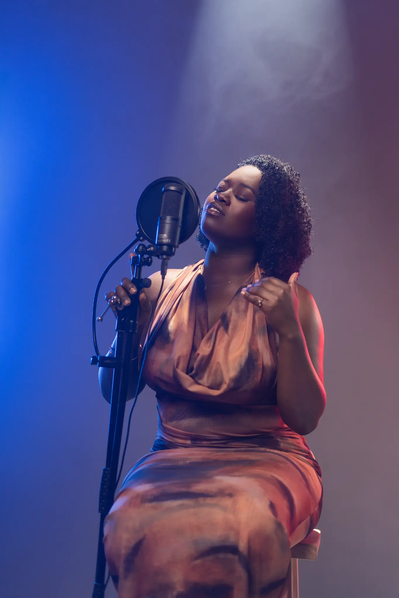 Faith James performing into a microphone under blue and violet light